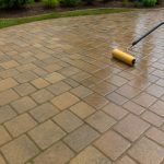 Close-up of a paint roller spreading wet sealer across paver stones.