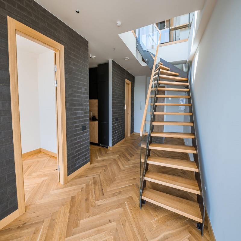 Modern home interior with herringbone hardwood flooring and open staircase, showcasing clean and well-maintained wood floors.